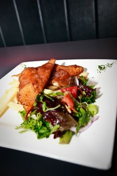 Serving of tasty golden chicken with fresh salads and French fries on a rectangular platter in a restaurant