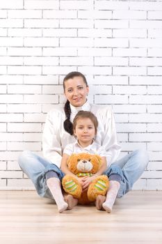 Mother and 5 year old daughter sitting by the wall, holding a toy