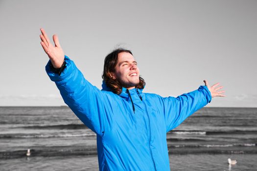 Happy man standing on the beach with hands up on black and white seascape. Concepts like overcoming depression etc.