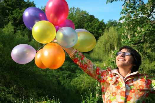 Smiling young woman with colourful balloons in the park