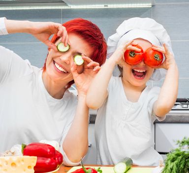 Mother and funny daughter playing in the kitchen with vegetables