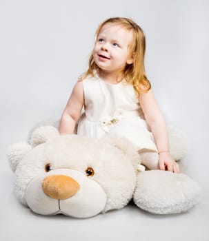 Little girl with toy bear on light background