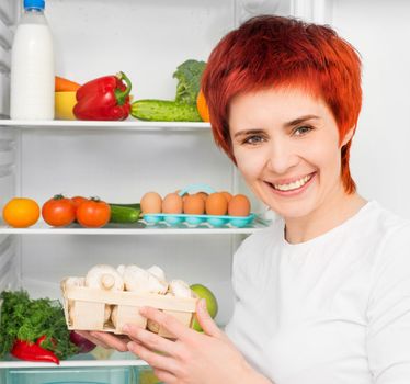 young smiling woman with mushroom against the refrigerator with food