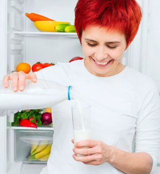 young woman with bottle milk and glass against the refrigerator with food