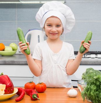 little girl in a cap chef in the kitchen with cucumbers