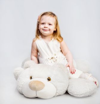 Little girl with toy bear on light background