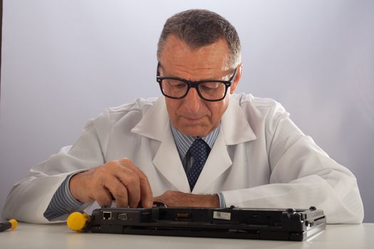 An older male wearing a white lab coat and repairing electronic equipments, like a technician or a repair man.