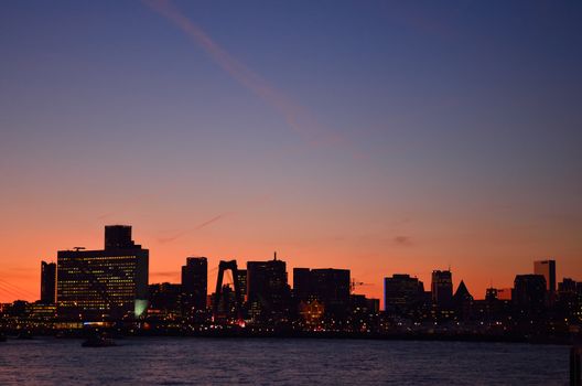 The skyline of the city of Rotterdam in the Netherlands over the water of the Maas river during sunset.