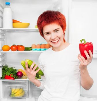 young woman with papper and cucumbers against the refrigerator with food