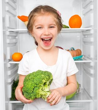 little girl with broccoli against a refrigerator with food