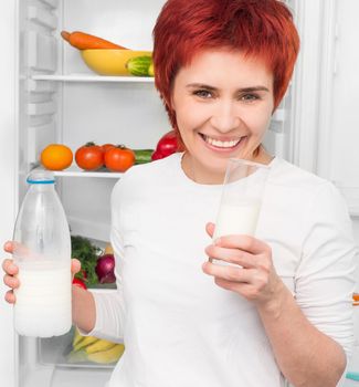 young woman with bottle milk against the refrigerator with food