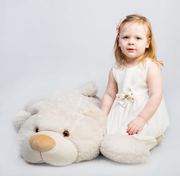 Little girl with toy bear on light background