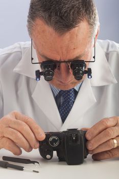 An older male wearing a white lab coat and repairing electronic equipments, like a technician or a repair man.