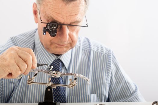 An older man wearing a shirt and tie, repairing a watch.