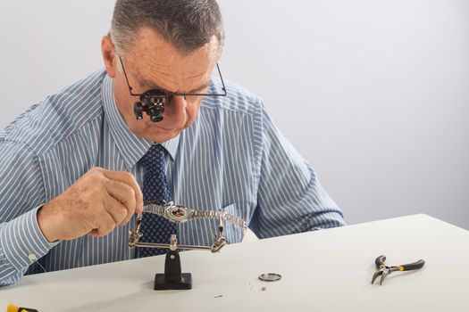 An older man wearing a shirt and tie, repairing a watch.