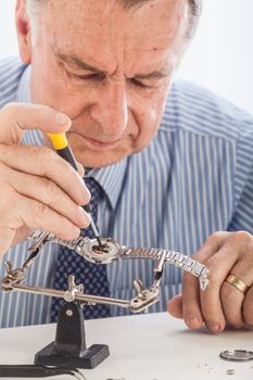 An older man wearing a shirt and tie, repairing a watch.