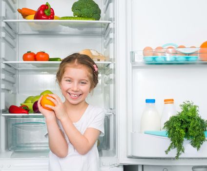 little girl with orange against a refrigerator with food