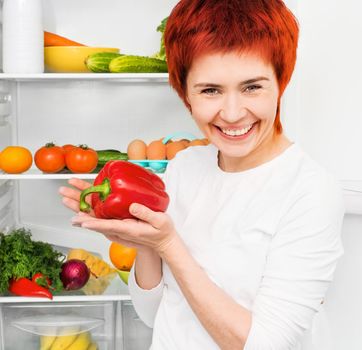 young smiling woman with papper against the refrigerator with food