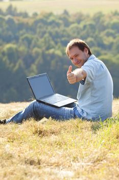 young man using laptop sitting on the grass on the hillside