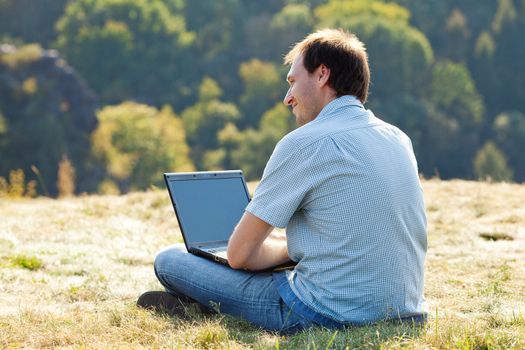 young man using laptop sitting on the grass on the hillside