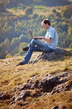 young man using laptop sitting on the grass on the hillside