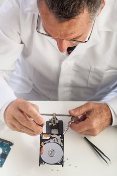 An older male wearing a white lab coat and repairing electronic equipments, like a technician or a repair man.