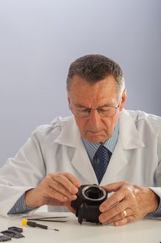 An older male wearing a white lab coat and repairing electronic equipments, like a technician or a repair man.