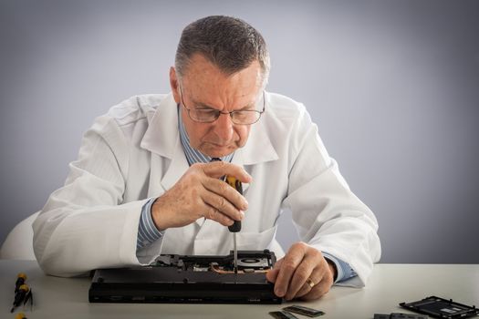 An older male wearing a white lab coat and repairing electronic equipments, like a technician or a repair man.