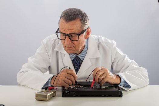 An older male wearing a white lab coat and repairing electronic equipments, like a technician or a repair man.