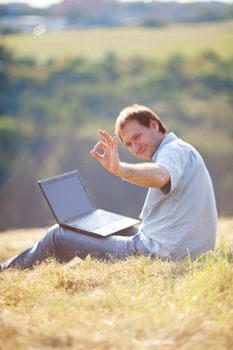 young man using laptop sitting on the grass on the hillside