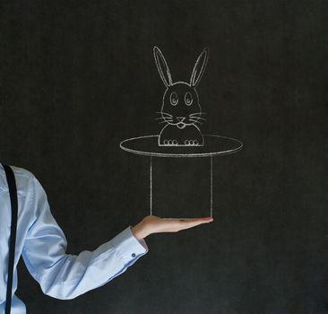Business man, student or teacher pulling a rabbit from a magic hat on blackboard background