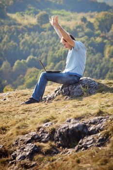 young man using laptop sitting on the grass on the hillside