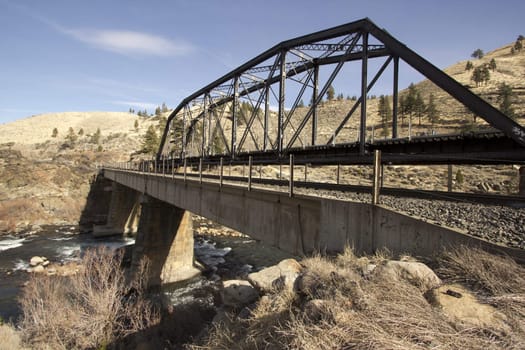 A train bridge in fall with blue skies and a river