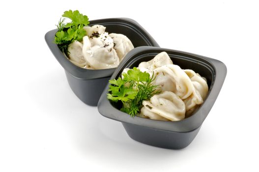 Meat pelmeni with sour cream and greens in black bowls isolated on white background