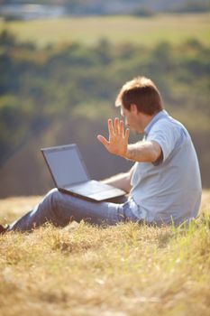 young man using laptop sitting on the grass on the hillside