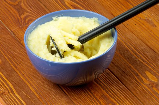 Tasty Mashed Potato with Potato Masher in Blue Bowl on Wooden background