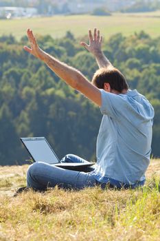 young man using laptop sitting on the grass on the hillside