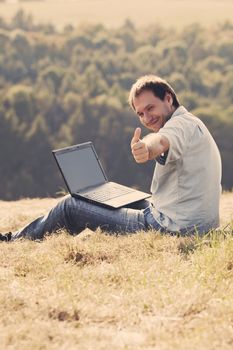 young man using laptop sitting on the grass on the hillside