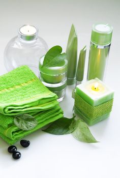 Creams for body care, candles and a green towel on a white background