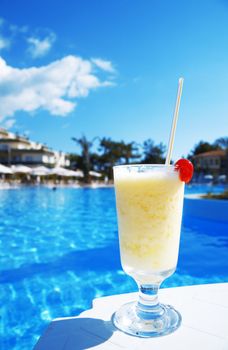 cocktail in glass with a cherry on a background blue water of pool