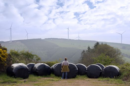 woman checking plastic wrapped bales with background windmills on lush irish countryside landscape in glenough county tipperary ireland