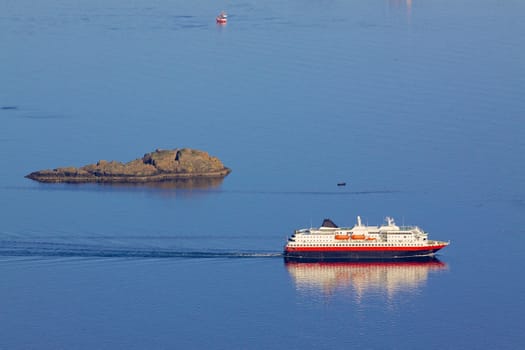 Large passenger ship sailing by tiny rock island on norwegian coast