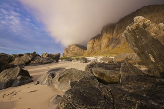 Rocks on the beach and scenic coastal cliffs on island Vaeroy on Lofoten islands in Norway
