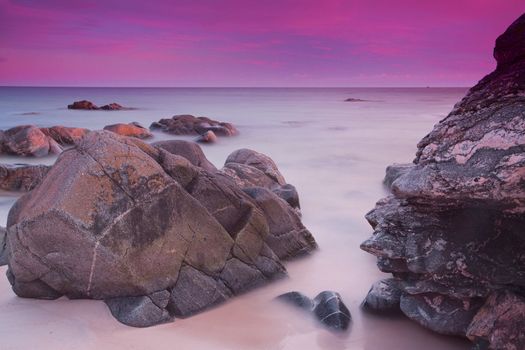 Long exposure of purple evening skies over ocean with large rocks near the shore