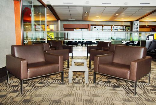 Modern waiting area with brown leather chairs, tables at an international airport with shops and treadmill.