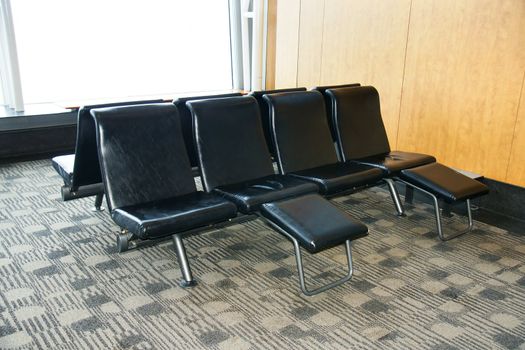 Comfortable waiting area at the airport with brown leather seats with foot rest and geometric carpet.