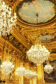 Opulent cristal chandeliers and gold leaves wood carved and painted ceiling, part of a french historical building, Lyon, France.