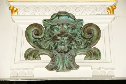 Great architectural detail above a door of an old european historical building of an ornate sculpted wooden lion head painted verdigris with gold leaves.