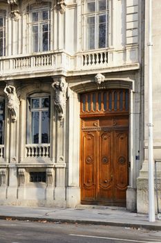 Beautiful wooden door of an old european apartment of flat stone building, with carved statues and balconies, Lyon, France.