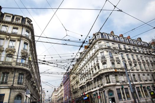 Modern public transportation with tramway or trolley cables criss-crossing at a busy street intersection contrasting with the old historic building architecture of European city, Lyon, France.